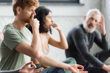 Kızıl saçlı adam yoga stüdyosunda burun deliğiyle nefes almaya çalışıyor. 