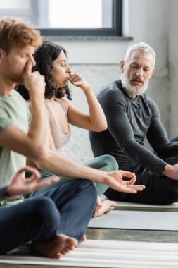 Ortadoğulu bir kadın yoga stüdyosunda, olgun bir koçun yanında burun deliği solunumu yapıyor. 