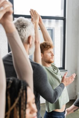 Olgun koç, yoga stüdyosunda kızıl saçlı adamın yanında Crescent Lunge Asana taklidi yapıyor. 