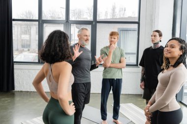 Orta yaşlı koç yoga stüdyosunda ırklar arası insanlarla konuşuyor. 