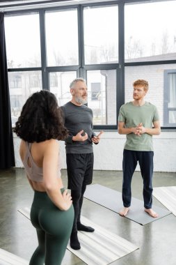 Middle aged coach talking to group of people in yoga studio  clipart