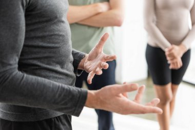 Olgun koçun yoga sınıfında bulanık bir grubun yanında el kol hareketi yapması. 