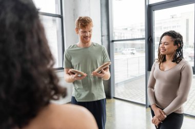 Smiling man looking at sadhu board near interracial group in yoga class  clipart