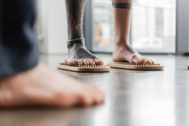 Yoga stüdyosunda çivi tahtasında çıplak ayakla duran dövmeli adam görüntüsü.