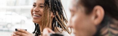 Neşeli Afro-Amerikalı kadın. Rasta saçlı, elinde Çin fincanı, dövmeli bir adamın yanında, bulanık önplanda, pankartta... 