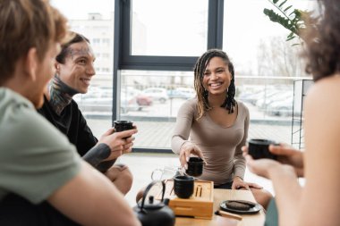 Neşeli çok kültürlü insanlar yoga stüdyosunda Puer içerken geleneksel çay fincanlarını tutuyorlar. 