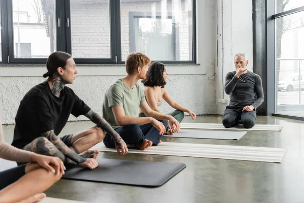 Coach showing nostril breathing technique to interracial group in yoga class