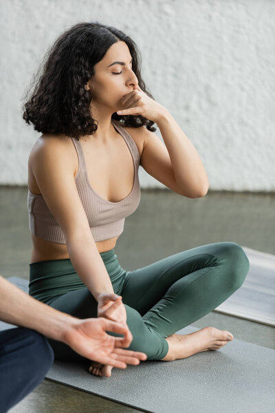 Middle eastern woman in sportswear practicing gyan mudra and nostril breathing in yoga studio 