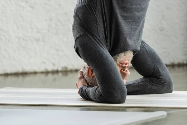 stock image Mature man doing Supported Headstand asana on mat in yoga studio 