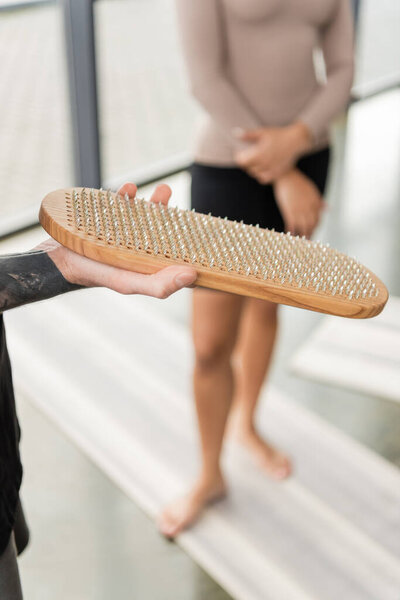 Cropped view of tattooed man holding sadhu board near blurred african american woman in yoga studio 
