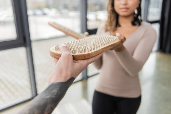 Cropped view of tattooed man giving sadhu board to african american woman in yoga class 