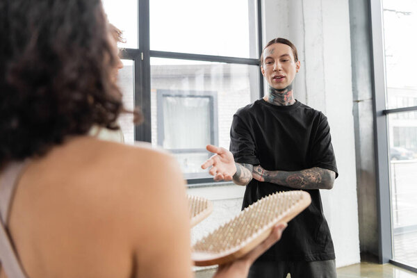 Young tattooed man talking to blurred woman with sadhu board in yoga class 