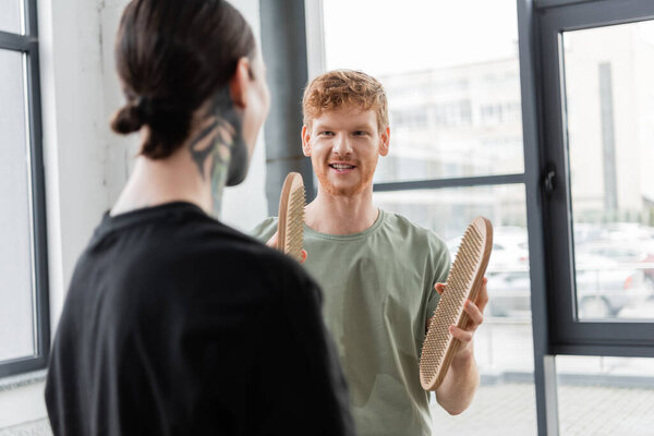 Smiling man holding sadhu board and talking to blurred friend in yoga studio 