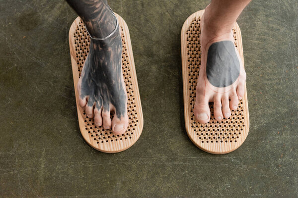 вид сверху на обрезанного человека с татуированными ногами, стоящего на доске для ногтей Садху 