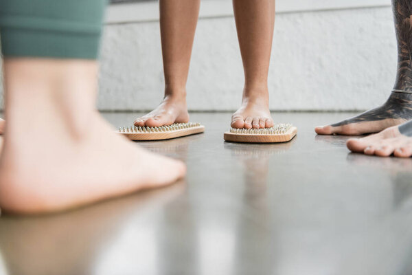 cropped view of woman standing on sadhu nail board near tattooed man in yoga studio 