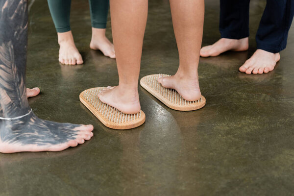 cropped view of woman standing on sadhu nail board near tattooed man and people in yoga studio 