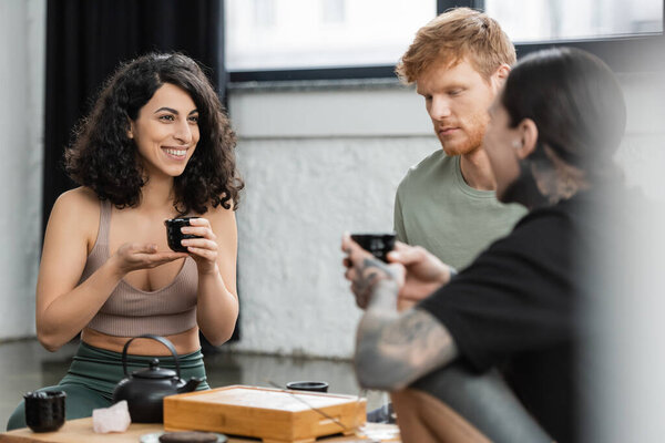 happy middle eastern woman having tea ceremony with people in yoga studio 