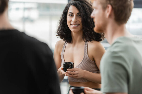 middle eastern woman with curly hair smiling during tea ceremony in yoga studio 