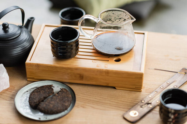 compressed pu-erh tea near Chinese teapot and incense stick on wooden stand 