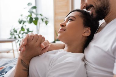 Mutlu Afrikalı Amerikalı kadının yatak odasında gülümseyen sakallı adamla el ele tutuşması.