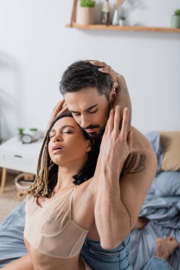 Sakallı, dövmeli bir adam, tutkulu bir Afrikalı Amerikalı kadının yanında, yatak odasında seksi iç çamaşırlarıyla.