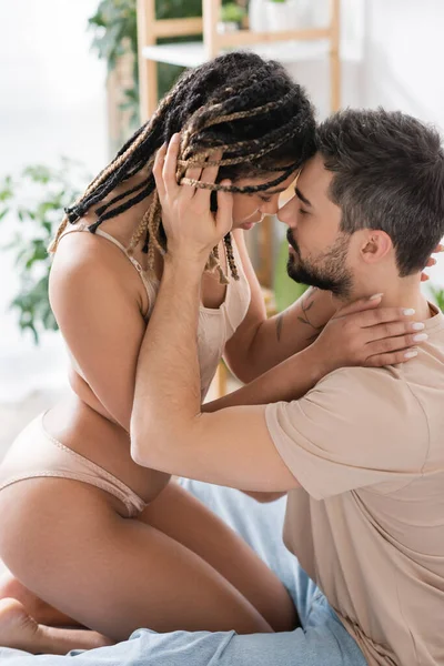 穿着性感女士内衣的充满热情的非洲裔美国女人在家里卧室里穿着T恤衫的褐发男人旁边的侧面形象 — 图库照片