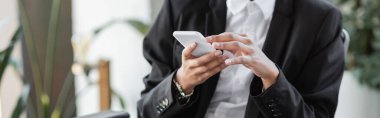 Siyah ceketli Afro-Amerikan iş kadınının ofiste cep telefonuyla sohbet edişinin kırpılmış görüntüsü.