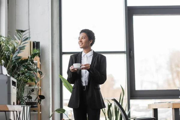 Επιτυχημένη Αφροαμερικανίδα Επιχειρηματίας Μαύρο Κοστούμι Κοιτάζει Μακριά Ενώ Στέκεται Φλιτζάνι — Φωτογραφία Αρχείου