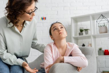 Psychologist in eyeglasses talking to distracted preteen patient in consulting room  clipart
