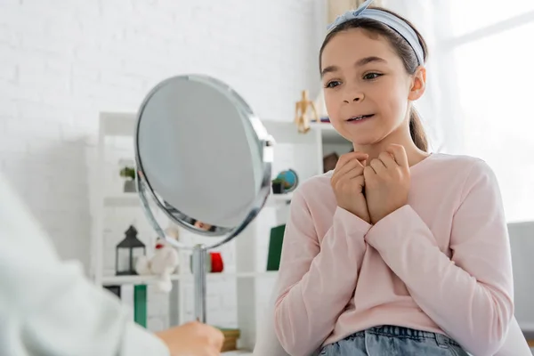 Smiling preteen kid looking at mirror near speech therapist in consulting room