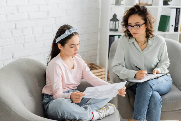 Ребенок проводит тест Роршаха и разговаривает с психологом с планшетом в консультационной комнате 