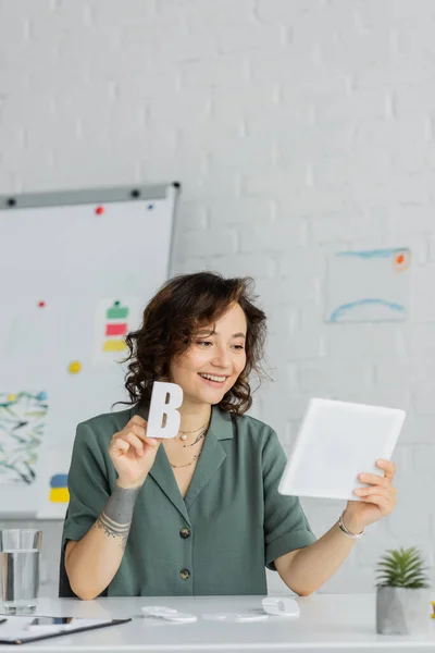 stock image Smiling speech therapist holding letter b during video call on digital tablet 