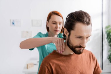 Bulanık osteopat muayene odasında muayene sırasında sakallı adamın acı dolu boynuna dokunuyor.