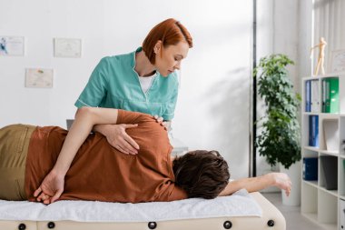 Osteopat rehabilitasyon sırasında yaralı adama omuz masajı yapıyor.