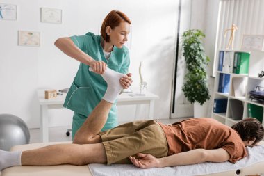 Osteopat, masaj odasında masaj masasında yatan bir adamın acı dolu ayaklarına masaj yapıyor.