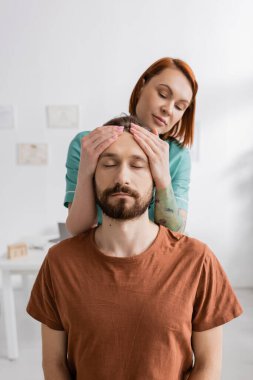 physiotherapist examining injured bearded man in consulting room clipart