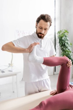 Fizyoterapist rehabilitasyon merkezinde yaralı bir kadının bacağıyla iyileşme manipülasyonu yapıyor.