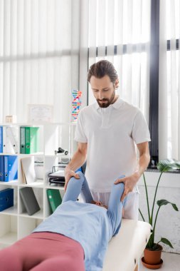Sakallı manuel terapist rehabilitasyon kliniğinde kadınlara kol masajı yapıyor.