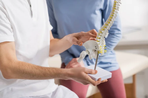 リハビリテーションセンターの患者の近くで脊椎モデルを保持する骨粗しょう症の部分的見解 — ストック写真