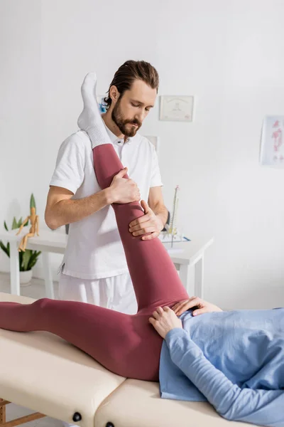 リハビリセンターで疼痛緩和療法中に女性の足を伸ばす理学療法士 — ストック写真