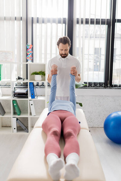 bearded manual therapist stretching arms of woman during recovery manipulation in modern rehabilitation center