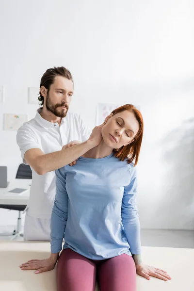 红头发妇女 靠近胡须理疗师 在会客室检查疼痛的颈部 — 图库照片