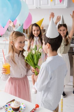 Bir bardak meyve suyu içen mutlu bir kız bulanık arka planda arkadaşlarının yakınındaki bir çocuktan lale alıyor. 