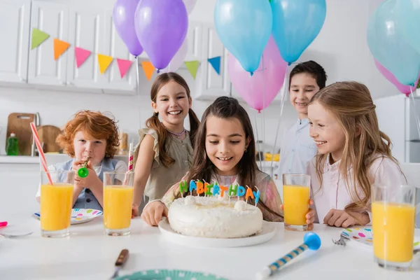お祝いの席でお友達のグループの近くでお誕生日ケーキを見ている陽気な女の子 — ストック写真