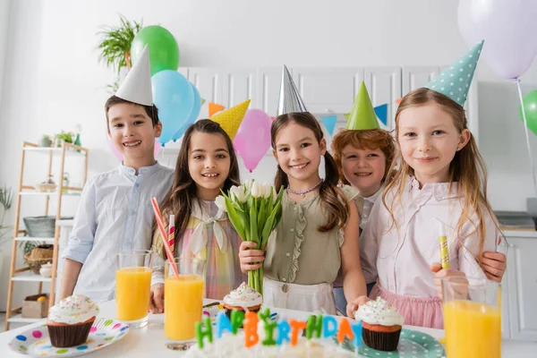 Wesoła Dziewczyna Trzyma Tulipany Pobliżu Przyjaciół Podczas Urodzin Domu — Zdjęcie stockowe