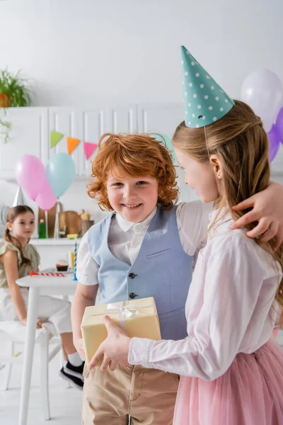 Glücklich Rotschopf Junge Umarmt Mädchen Mit Geschenk Während Geburtstagsparty — Stockfoto