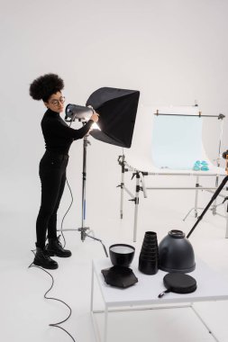 Afrikalı Amerikalı içerik üreticisi çekim masasının yanında projektör monte ediyor ve fotoğraf stüdyosunda ışıklandırma ekipmanları 