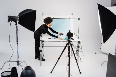 Modern fotoğraf stüdyosunda çekim masasının yakınındaki teşhir sayacı ve ışıklandırma ekipmanlarıyla Afro-Amerikan içerik üreticisi