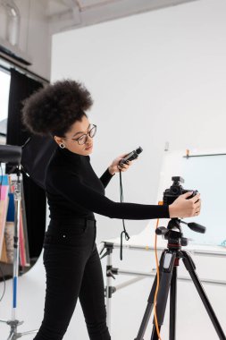 Afro-Amerikan içerik yapımcısı dijital kamerayı çağdaş fotoğraf stüdyosunda ayarlıyor.