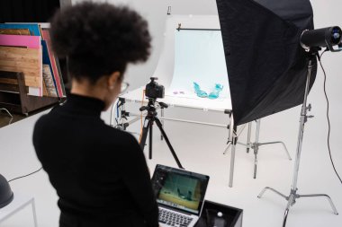 Fotoğraf stüdyosunda dizüstü bilgisayarla çalışan Afro-Amerikan içerik yöneticisinin arka görüntüsü